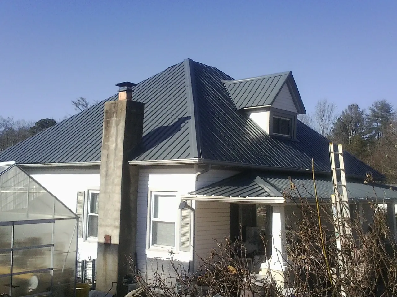 Dark blue standing seam metal roof on a white farmhouse with dormer — Slate & Tile Roof Repair by Roofing Brothers in Ankeny
