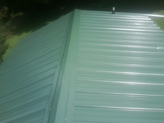 New green metal panels meeting at the ridge of a roof — Flat Roof Repair work by our crew in Ankeny