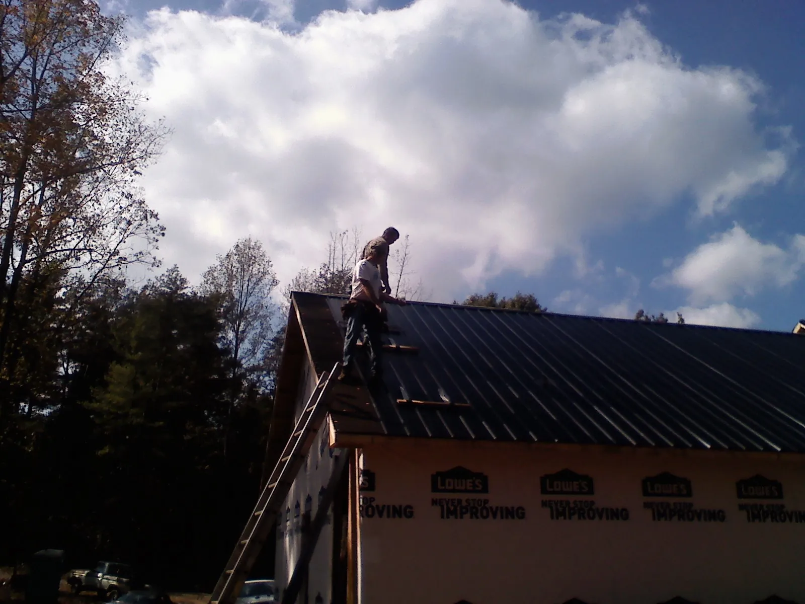 Roofer fastening dark metal panels high against a cloudy sky, from a Roof Inspection job in Ankeny