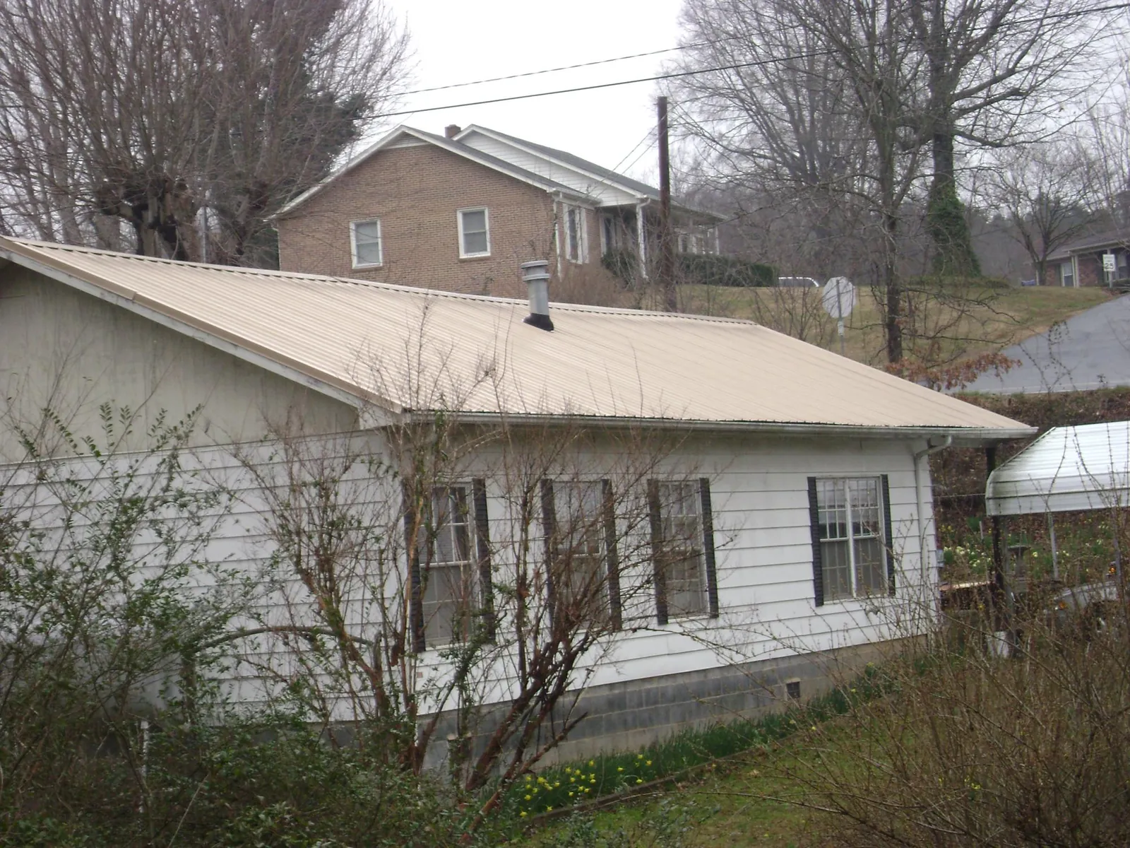 Tan metal roof on a white sided house set into a hillside — Commercial Roofing by Roofing Brothers in Ankeny