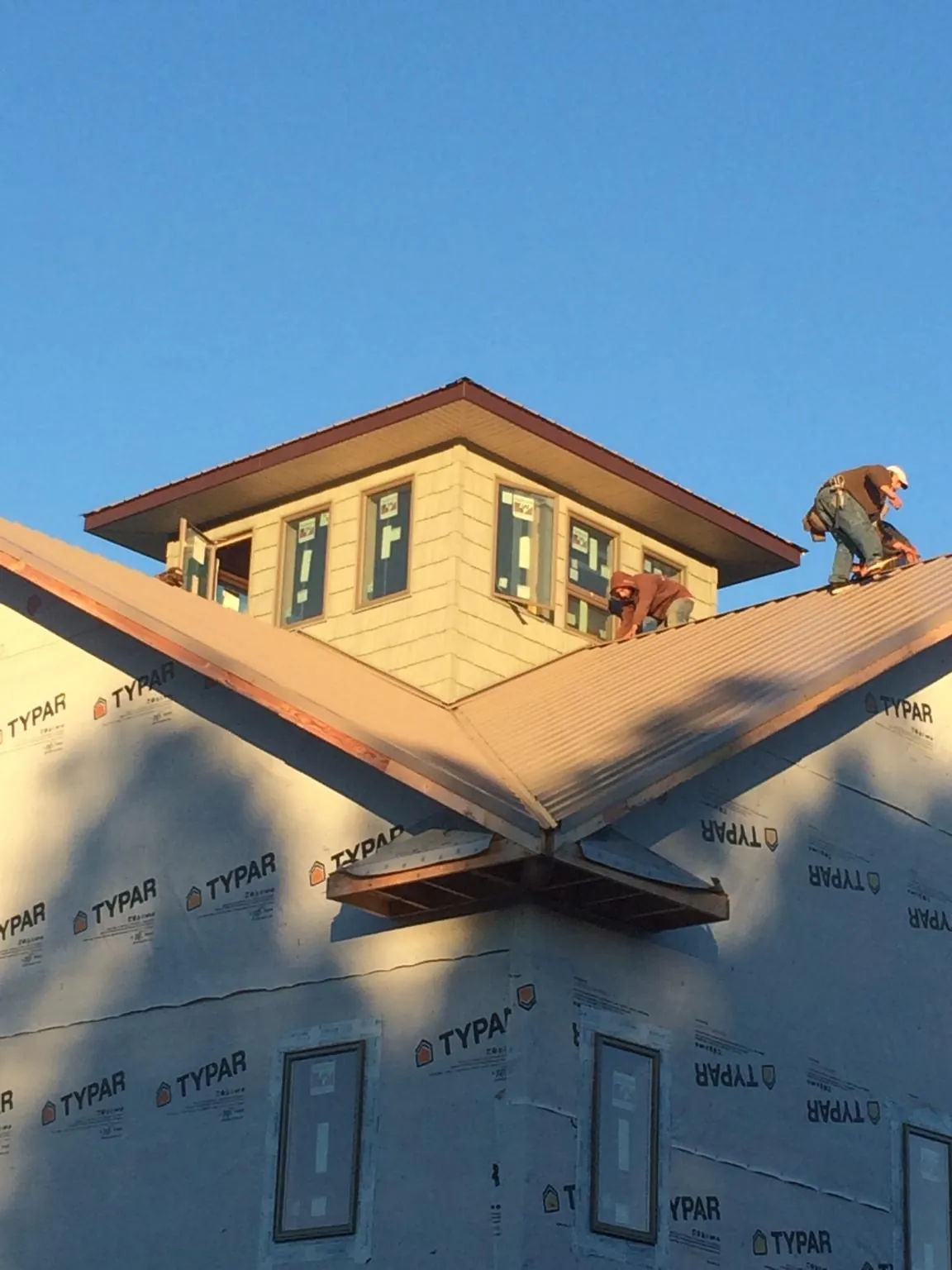 Roofers working around a rooftop cupola on a new metal roof at sunset — Roof Waterproofing in Ankeny by Roofing Brothers
